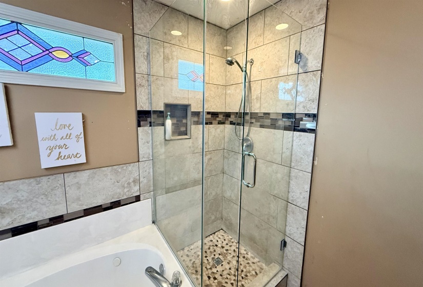 Glass-enclosed shower with pebble-tile flooring, tiled walls, and a recessed niche