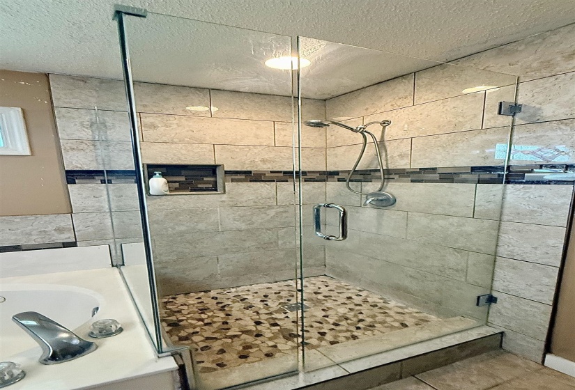 Frameless glass shower enclosure featuring a mosaic pebble floor, tiled walls with decorative accent band, built-in shower niche, and a chrome shower fixture