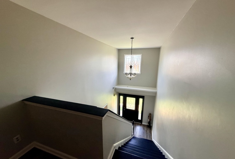 Two-story entryway featuring a decorative glass window, dark wood-finish flooring, and a classic chandelier