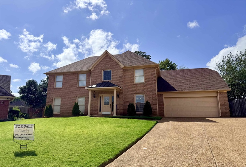 Brick exterior residence featuring a front porch with columns, a two-car garage, and a concrete driveway