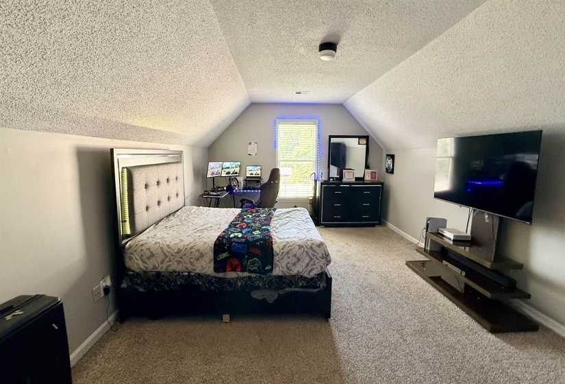 Spacious room featuring vaulted ceilings, neutral-toned carpeting, and a window providing natural light