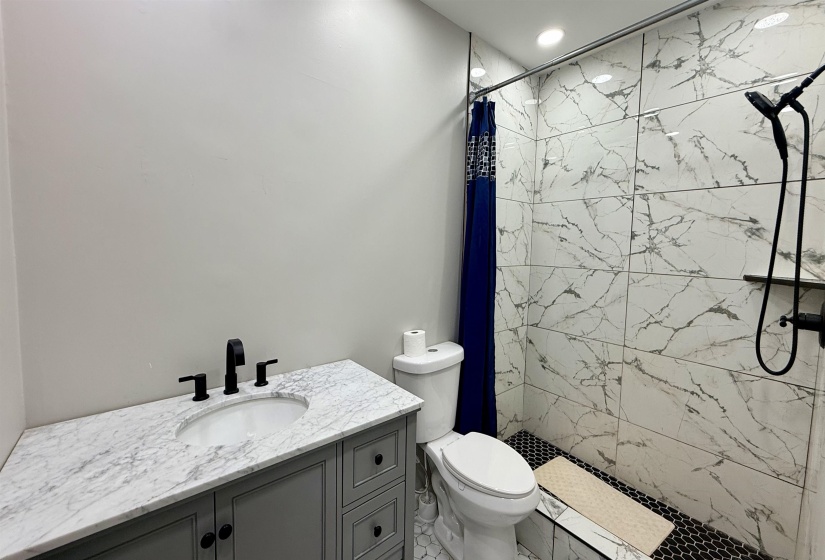 Bathroom featuring a walk-in shower with large format marble-look tile, black hexagonal tile shower floor, and a matte black shower fixture
