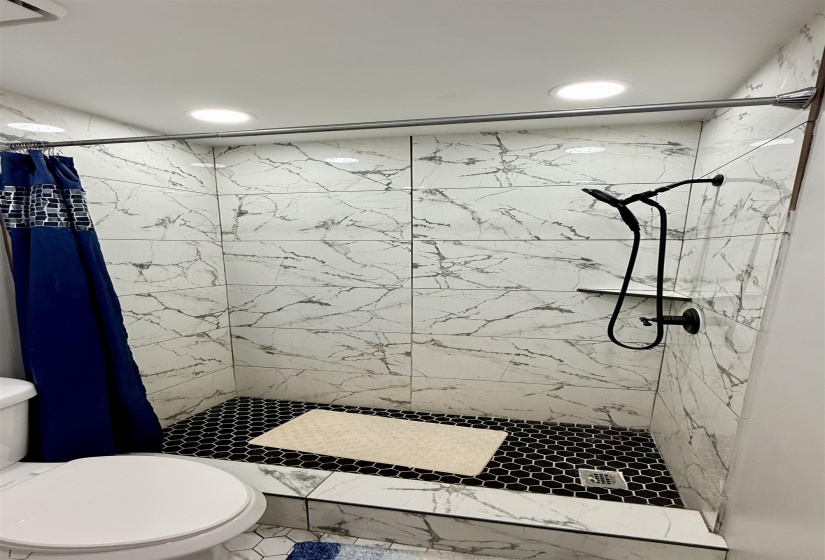 Shower with white marble-look subway tile walls, black hexagonal floor tiles, matte black shower fixtures, and recessed ceiling lighting