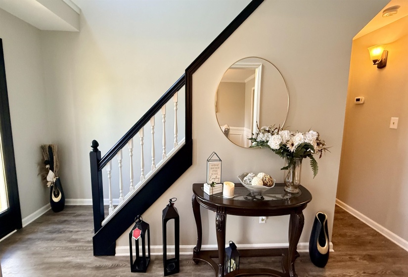 Entryway featuring wood-finish flooring, a staircase with dark newel posts and handrails, white balusters, and light-toned walls with white trim