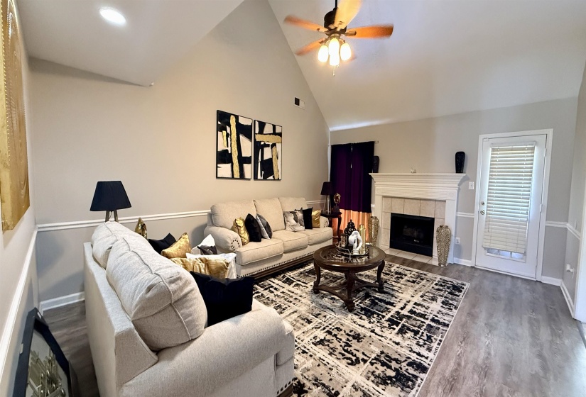 Living room featuring vaulted ceilings, wood-finish flooring, a white mantel fireplace with tile surround, and a ceiling fan with light fixture