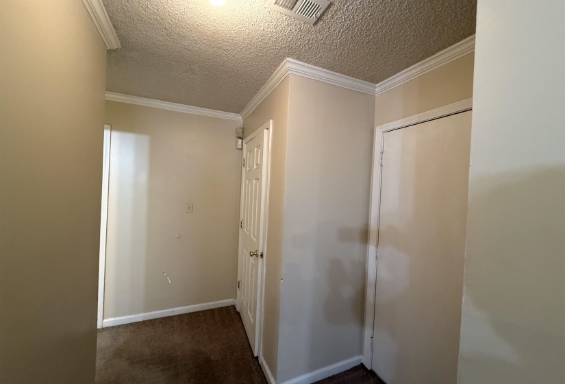 Hallway featuring neutral wall tones, crown molding, and a textured ceiling