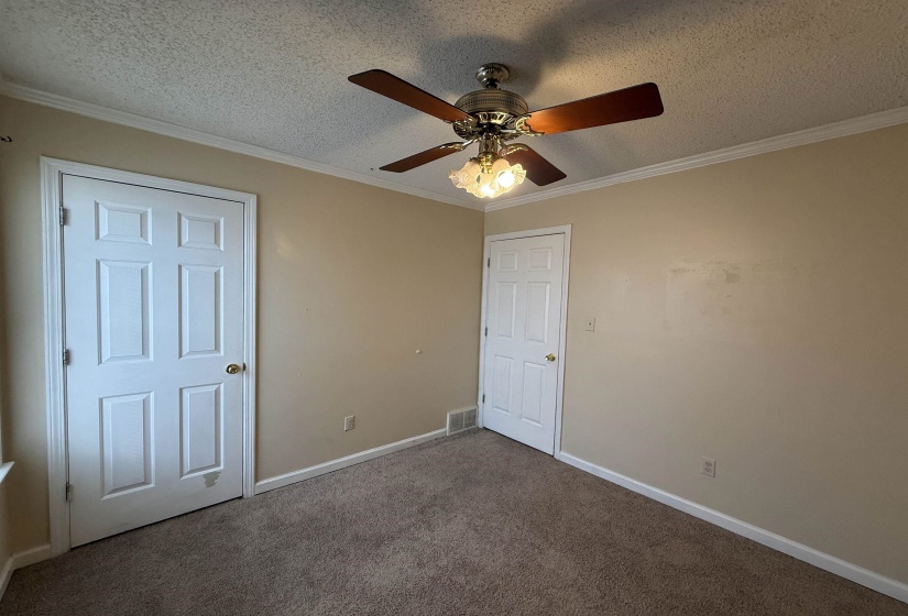 Neutral-toned room featuring a ceiling fan with light fixture, textured ceiling, and crown molding