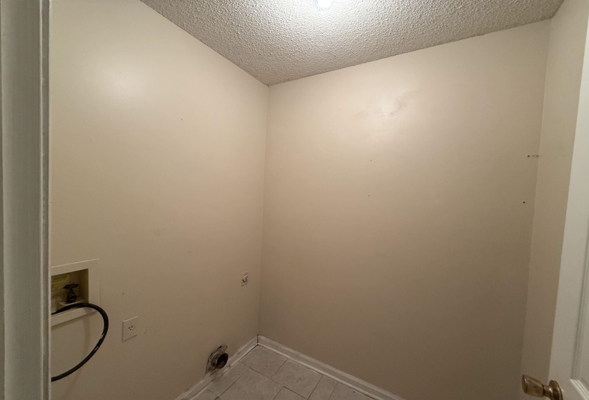 Dedicated utility space featuring light-toned walls, a textured ceiling, and tiled flooring