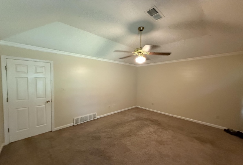 Carpeted room featuring a ceiling fan with light, white crown molding, and a white six-panel door