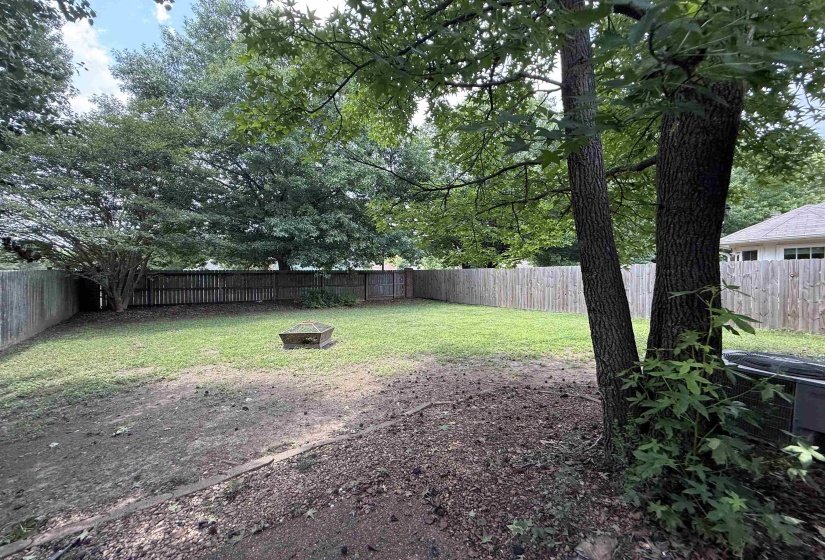 Expansive backyard featuring a wood privacy fence, mature trees, and a central planter box