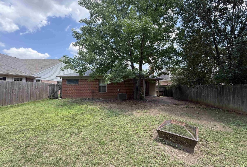 Expansive backyard featuring a mature shade tree, full privacy fencing, and a brick exterior home with an outdoor covered patio