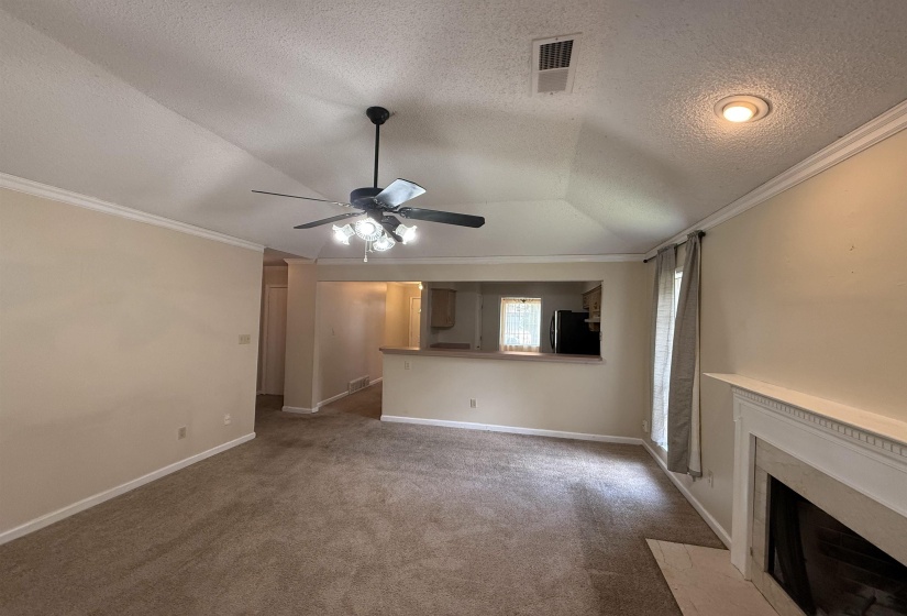 Carpeted living space featuring a white mantel fireplace, vaulted ceiling, and crown molding