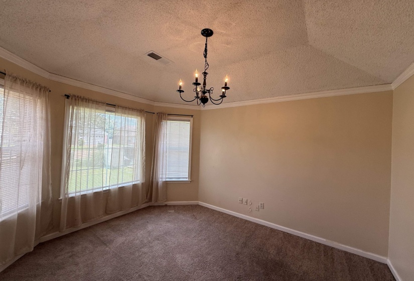Spacious room featuring a bay window, crown molding, a decorative chandelier, and neutral carpet flooring
