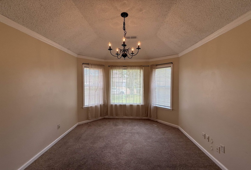 Bay window room featuring a black chandelier, crown molding, neutral wall paint, and textured carpet flooring