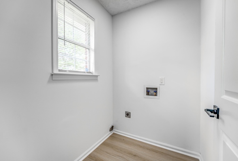 Dedicated laundry area featuring a window with blinds, wood-finish flooring, and crisp white walls