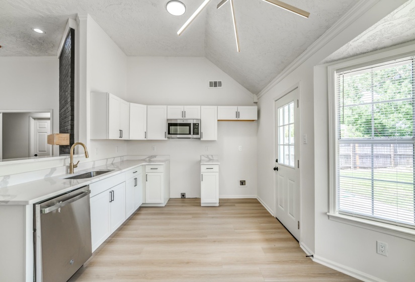 Kitchen featuring white cabinetry, light-toned wood-finish flooring, stainless steel dishwasher, and a contemporary gold-finish faucet