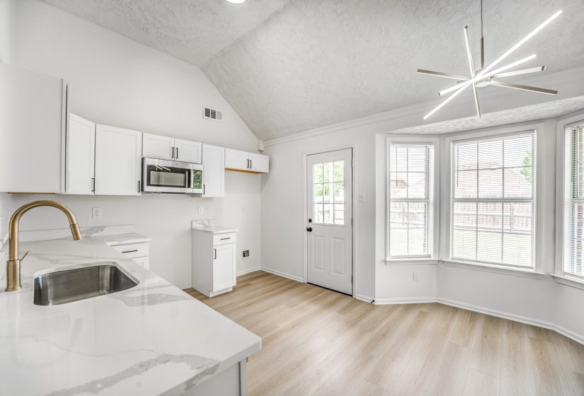 Kitchen featuring white cabinetry, stainless steel microwave, and a gold-finish faucet