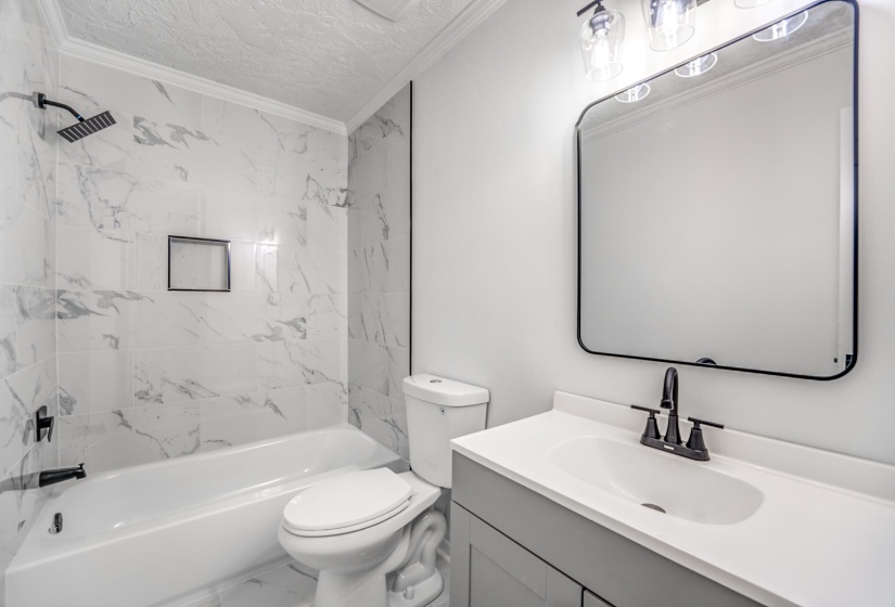 Modern bathroom featuring a white bathtub with marble-look tile surround and a matte black shower head