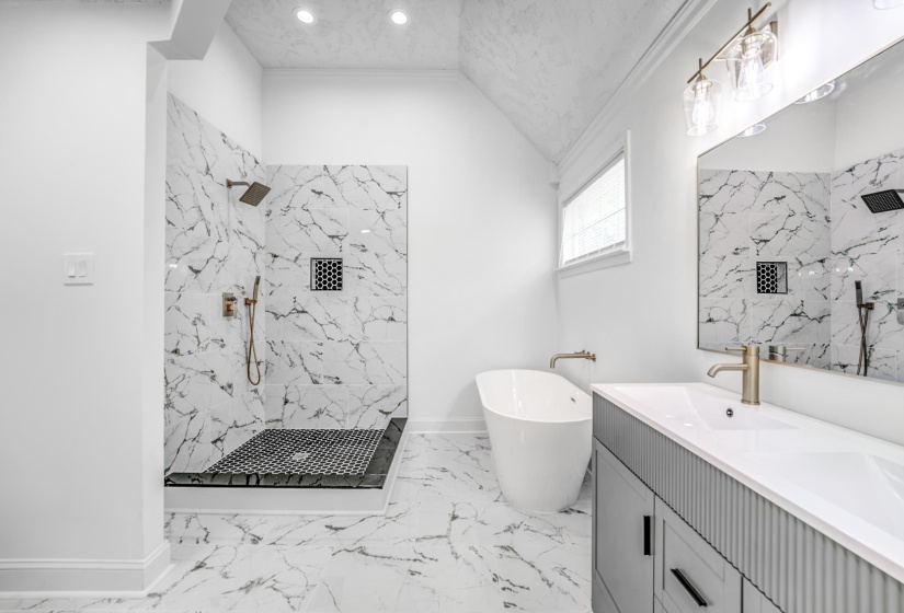 Spacious bathroom featuring a freestanding soaking tub, a walk-in shower with patterned tile, a double vanity with a contemporary ribbed base, and recessed lighting