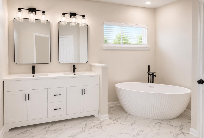 Bathroom featuring a freestanding soaking tub with a matte black floor-mounted faucet, a double vanity with white cabinetry and integrated sinks, and matte black hardware