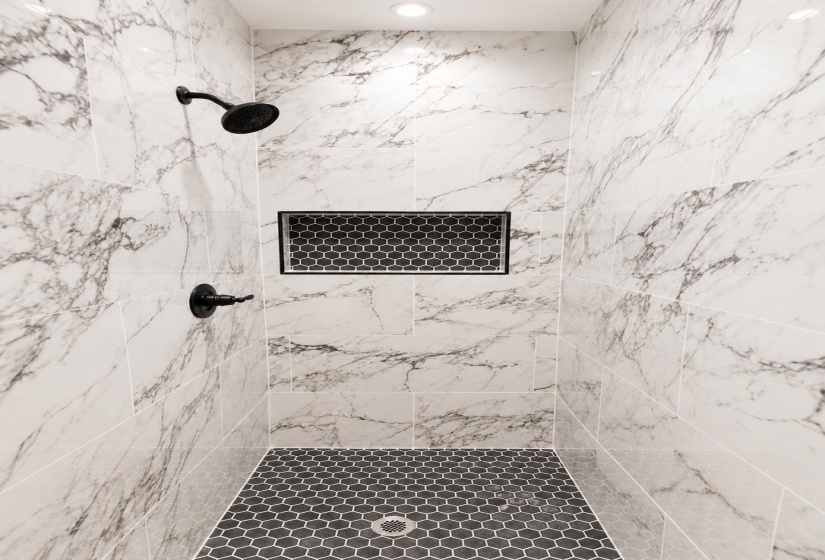 Walk-in shower featuring large format white and grey marbled tile walls, a recessed niche with black hexagonal tile, black hexagonal floor tiling, matte black shower fixtures, and a ceiling-mounted recessed light