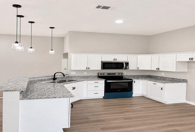 Modern kitchen featuring white shaker cabinetry, speckled countertops, stainless steel appliances, and wood-finish flooring