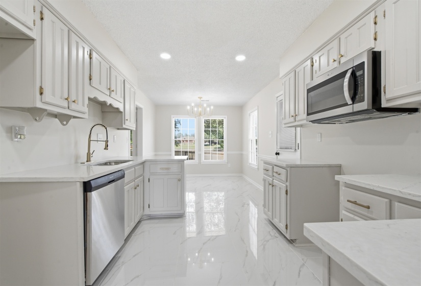 Kitchen featuring white cabinetry with gold-toned hardware, stainless steel appliances, white countertops, and white tile flooring