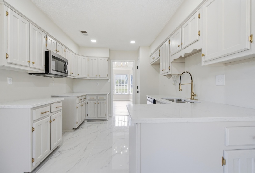 Bright kitchen featuring extensive white cabinetry with gold-toned hardware, white countertops, and white tile flooring