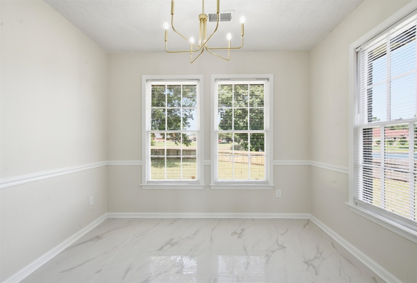 Interior space featuring three windows with white blinds, a gold-tone chandelier, and light-toned walls with chair rail molding