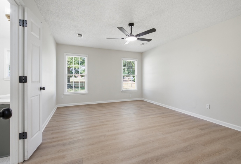 Spacious room featuring wood-finish flooring, two large windows, a modern ceiling fan with integrated lighting, white baseboards, and a neutral wall color