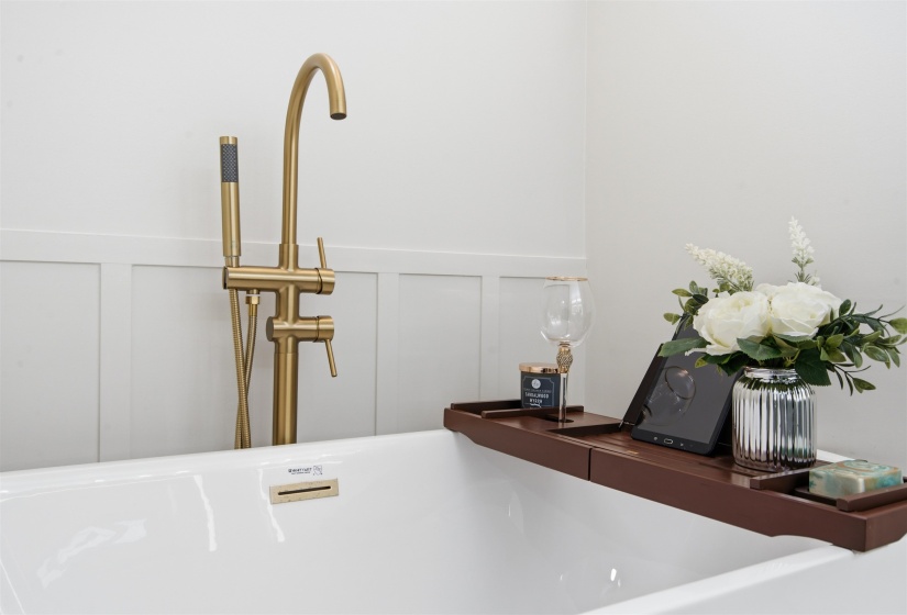 Freestanding soaking tub with a floor-mounted brushed gold faucet and hand shower