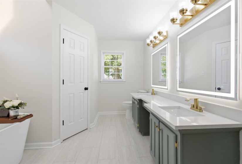 Bathroom featuring dual vanities with quartz countertops, integrated sinks, and gold-finish fixtures