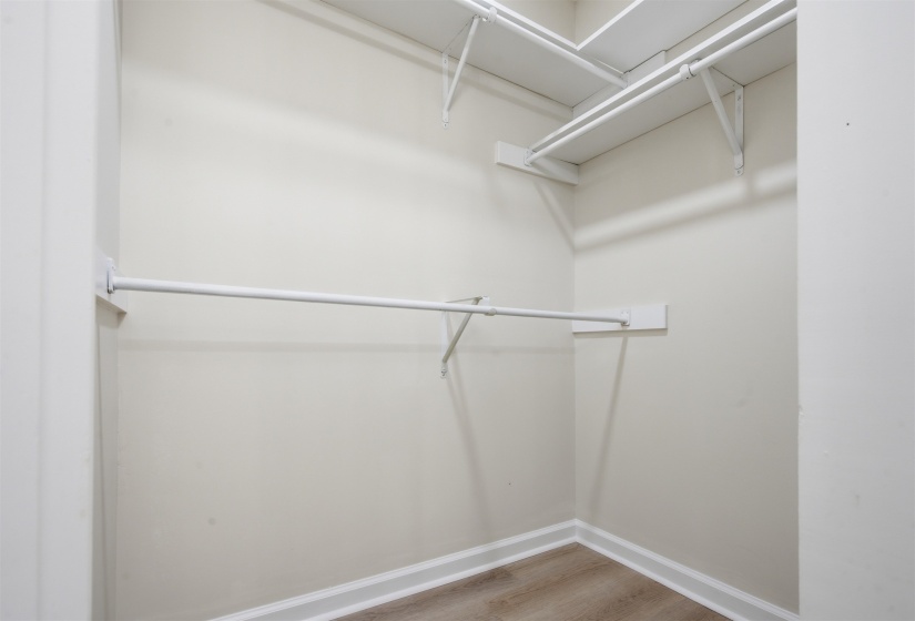 Corner closet featuring wood-finish flooring, white baseboards, and built-in white shelving