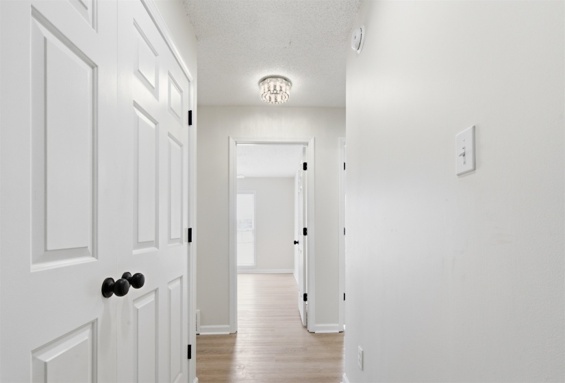 Hallway featuring light wood-finish flooring, white paneled doors with matte black hardware, and a decorative flush-mount ceiling light