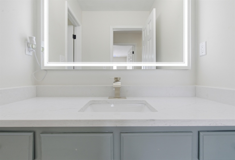 Backlit vanity mirror over a white countertop with an integrated rectangular sink and a polished chrome faucet