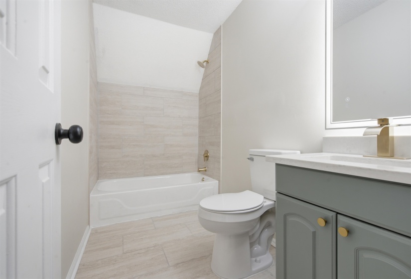 Bathroom featuring a white bathtub with gold-finish fixtures, light-toned wall tile surround, and coordinating floor tiles