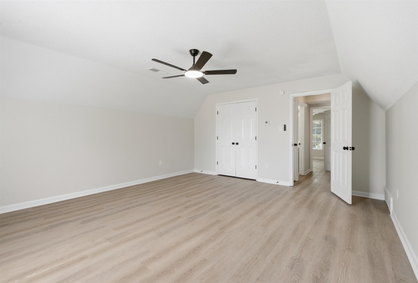 Spacious room featuring wood-finish flooring, a modern ceiling fan with integrated lighting, and crisp white baseboards