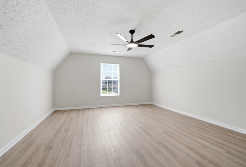 Spacious room featuring vaulted ceilings, light wood-finish flooring, and a contemporary ceiling fan