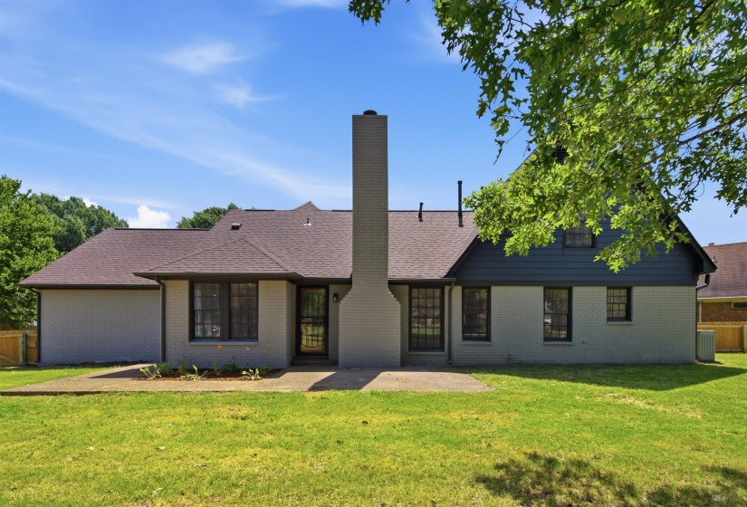 Rear exterior featuring a substantial brick chimney, a concrete patio, and a shingle roof