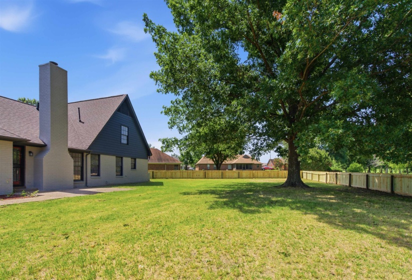 Expansive backyard featuring a mature shade tree, a newly installed wood privacy fence, and a brick exterior with a substantial chimney