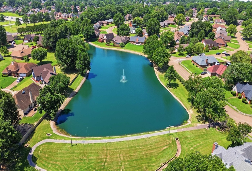 Lakeside community featuring a central pond with a fountain, surrounded by residential properties and mature trees