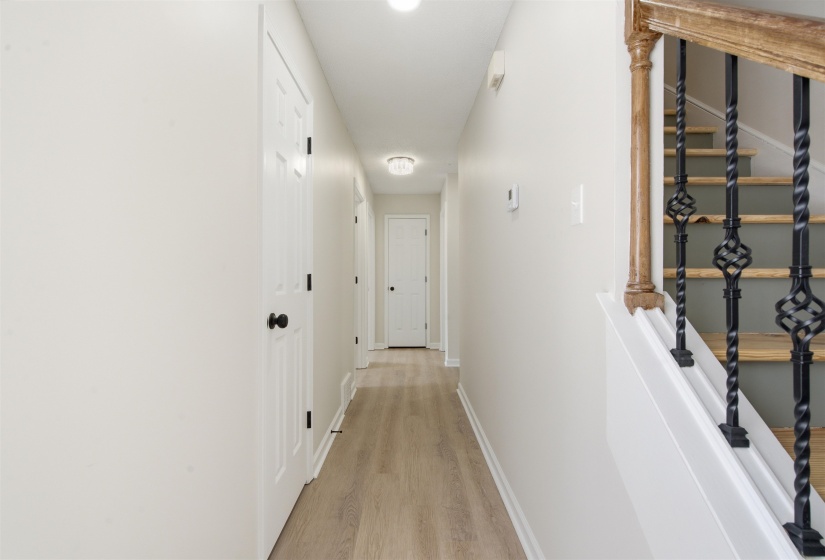 Hallway featuring wood-finish flooring, white paneled doors with black hardware, recessed lighting, and a staircase with an ornamental iron balustrade