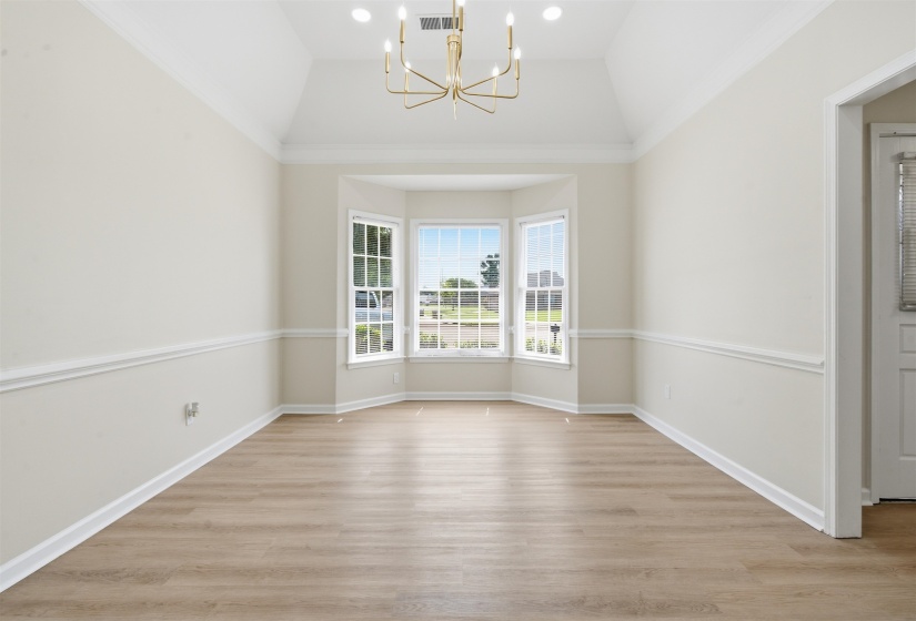 Spacious room featuring a bay window, wood-finish flooring, vaulted ceiling, and a contemporary chandelier
