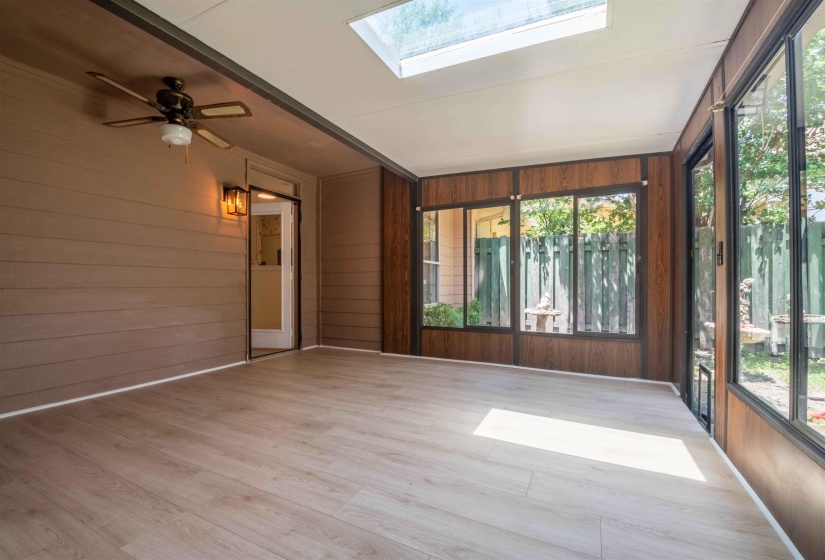 Enclosed sunroom featuring a skylight, light wood-finish flooring, and a ceiling fan