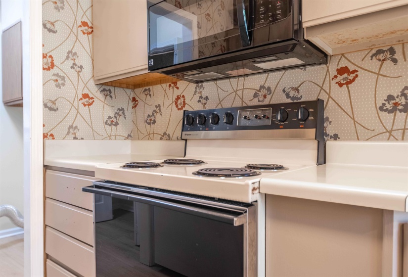 Kitchen featuring a built-in range, matching overhead microwave, neutral cabinetry, and floral patterned wall covering