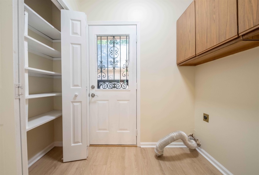 Utility space featuring light wood-finish flooring, built-in wooden cabinetry, a white panel door with decorative ironwork, and a built-in storage closet with shelving