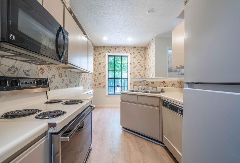 Kitchen featuring a built-in microwave, electric range, stainless steel sink, and wood-finish flooring