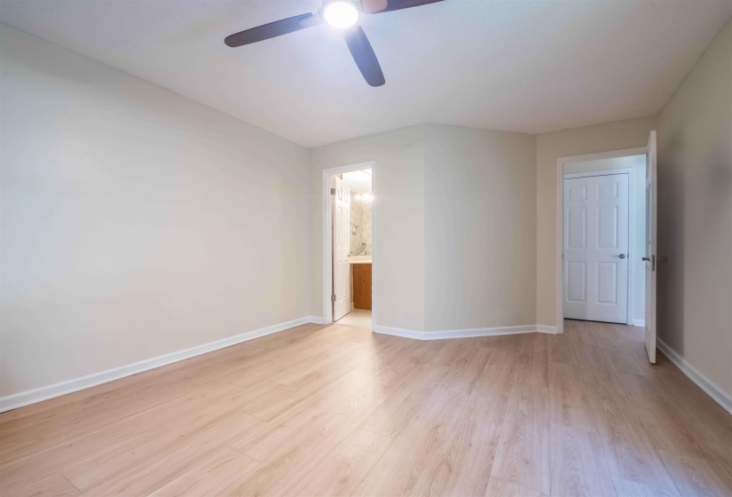 Spacious room featuring wood-finish flooring, light-toned walls, a ceiling fan, and white trim throughout