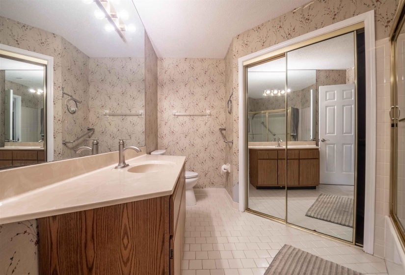 Bathroom featuring a spacious wood-finish vanity with a single basin, large wall-mounted mirror, and overhead strip lighting
