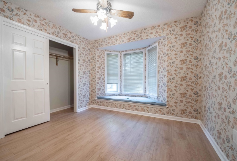Room featuring a three-panel bay window with integrated window seat, wood-finish flooring, and a ceiling fan with light fixture